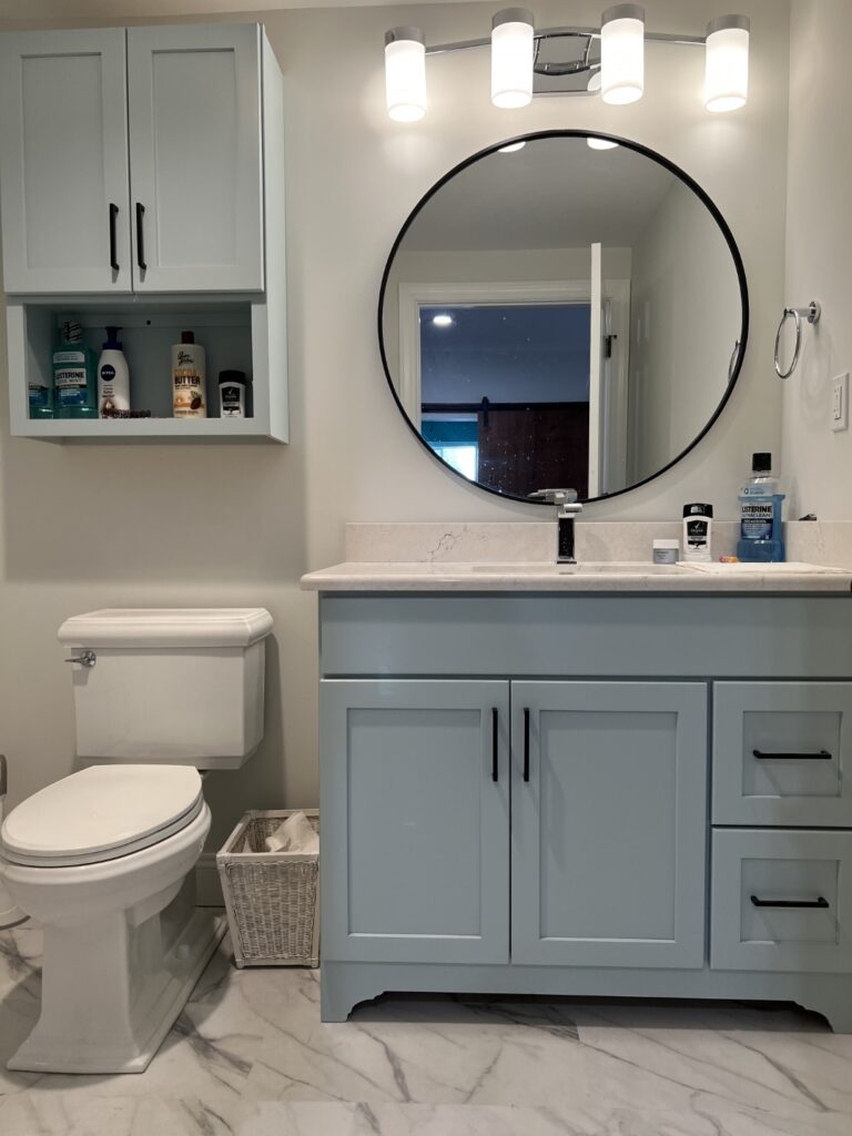 Bathroom in Linglestown, PA Basement Remodel from GP Harris with light grey flooring, a blue vanity, and large round mirror.